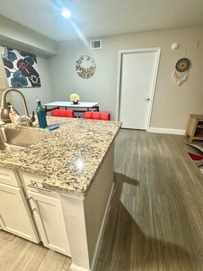 A kitchen with granite countertops, a sink, and a dining area with red chairs. - 2-bedroom apartment in beautiful Houston with AC and fitness room (Houston)