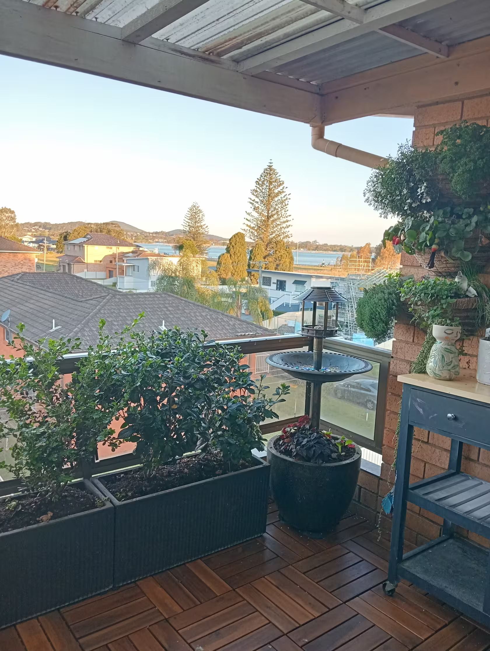 A balcony with a view of a residential area, a bird feeder, and potted plants.