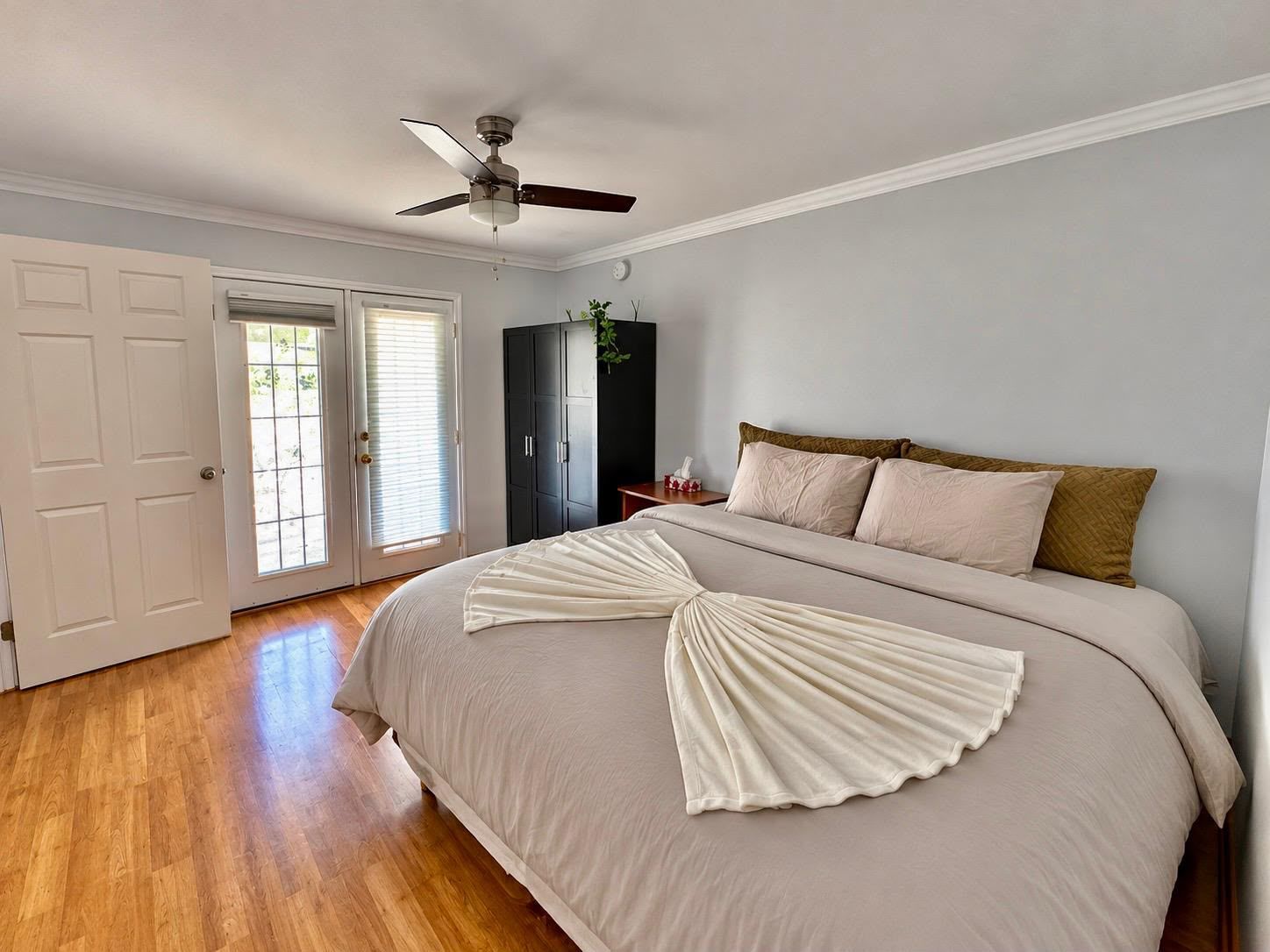 A bedroom with a bed, a ceiling fan, a wardrobe, and a door leading to a balcony.