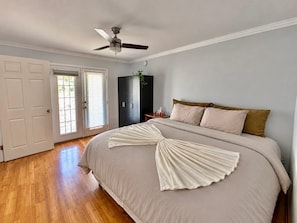 Une chambre à coucher comprenant un lit, un ventilateur de plafond, une armoire et une porte donnant sur un balcon.