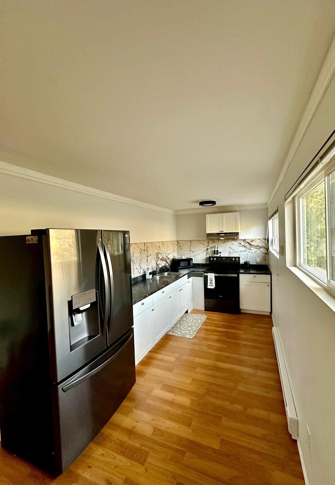 A modern kitchen with a stainless steel refrigerator, white cabinets, and a wooden floor.