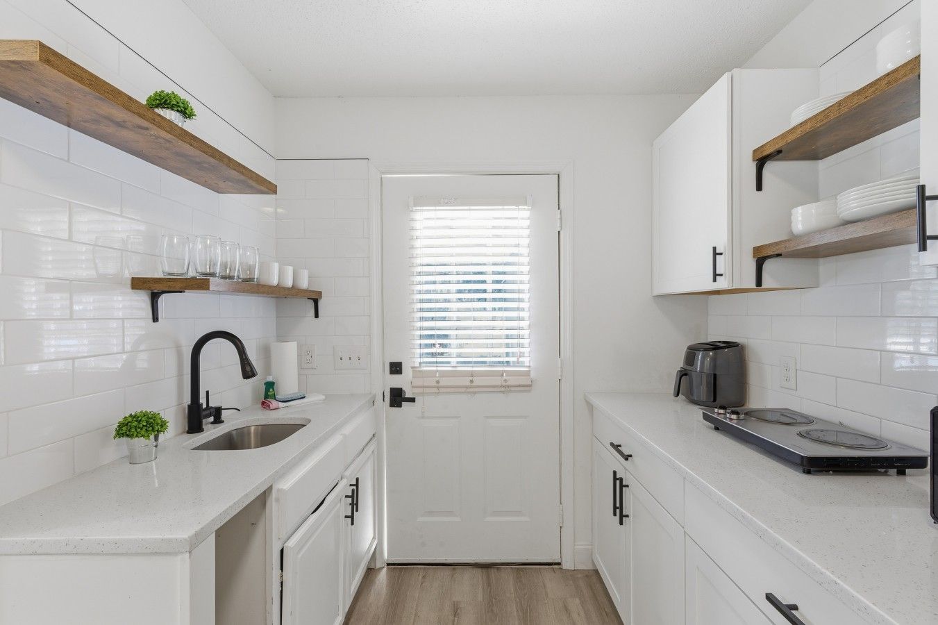 A compact kitchen with white cabinetry, a built-in stove, and a window with blinds.