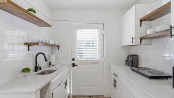 A compact kitchen with white cabinetry, a built-in stove, and a window with blinds.