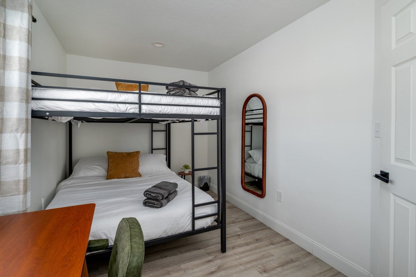 Habitación con literas, una mesa de madera, una silla verde y un espejo en la pared.