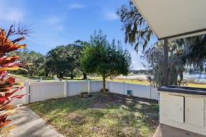 A backyard with a white fence, a tree, and a view of a lake.