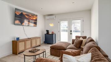 A living room with a brown sofa, a coffee table, a TV mounted on the wall, a cabinet, and a door leading outside.