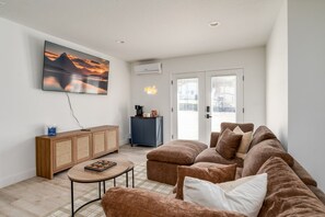 Un salon avec un canapé marron, une table basse, un téléviseur fixé au mur, un meuble et une porte donnant sur l’extérieur.