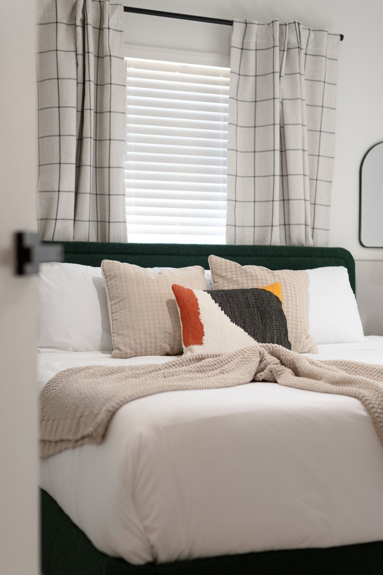 A bed with a green headboard, white bedding, and multiple pillows in various patterns and colors.