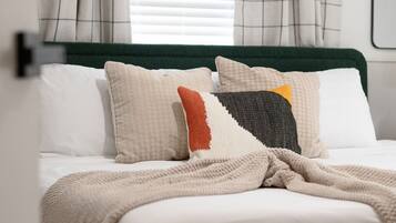 A bed with a green headboard, white bedding, and multiple pillows in various patterns and colors.