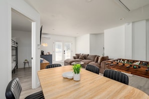 A modern living room with a sofa, a dining table with chairs, a coffee table with a plant, and a foosball table.