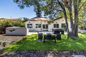 Uma casa moderna com um pátio, área de estar ao ar livre e uma banheira de hidromassagem.