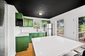 A modern kitchen with green cabinets, a white countertop, and a stainless steel refrigerator. - Lakeside Lakehouse & Bunkbed Cabin, Pool, Dock, Gameroom/All king beds &own bath (Spicewood)