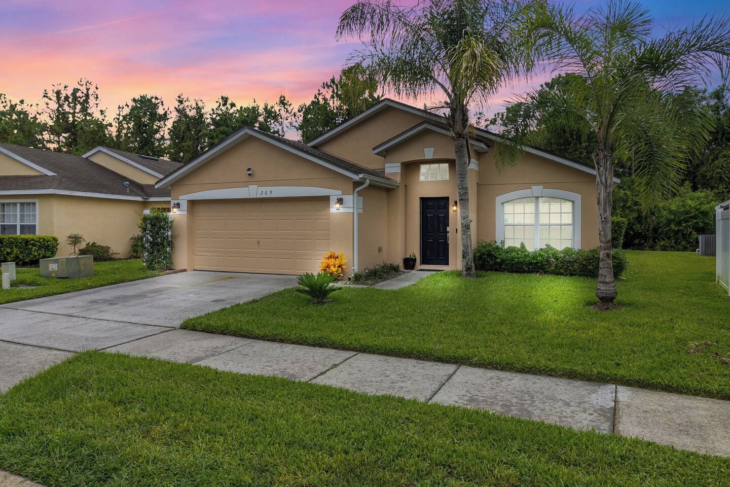 A residential house with a garage, a well-maintained lawn, and a palm tree.
