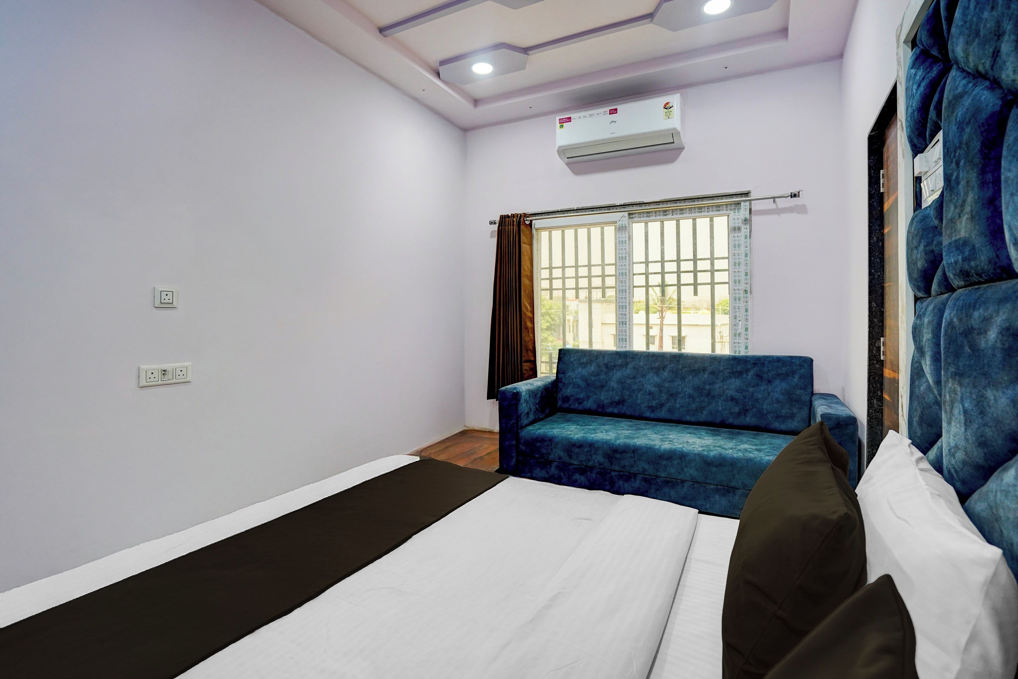 Une chambre d’hôtel avec un lit, un canapé bleu, une fenêtre avec des rideaux, un climatiseur et une prise électrique au mur.