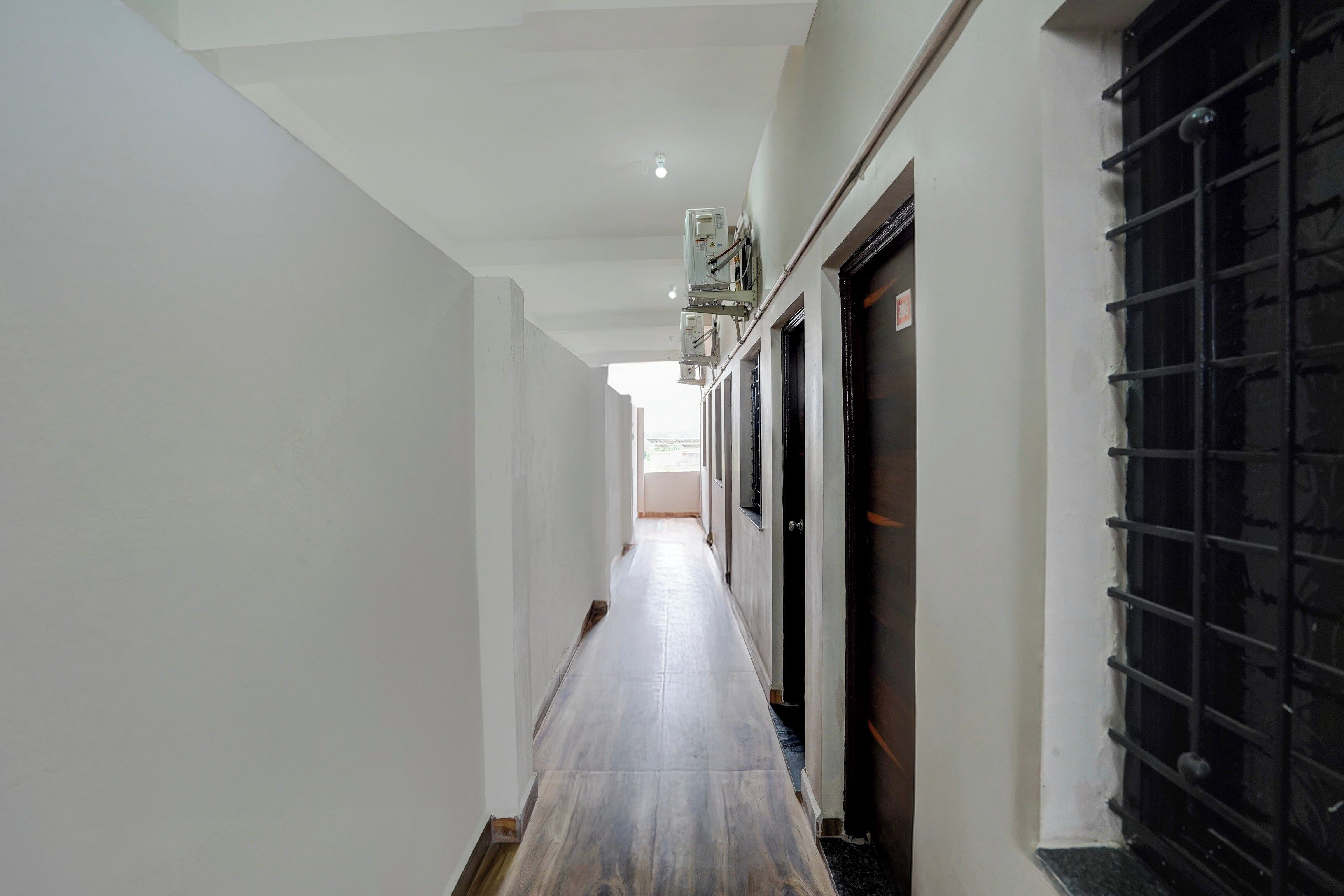 A hallway with a wooden floor, white walls, and a door with a black metal gate.