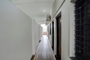 Un pasillo con suelo de madera, paredes blancas y una puerta con reja de metal negro.