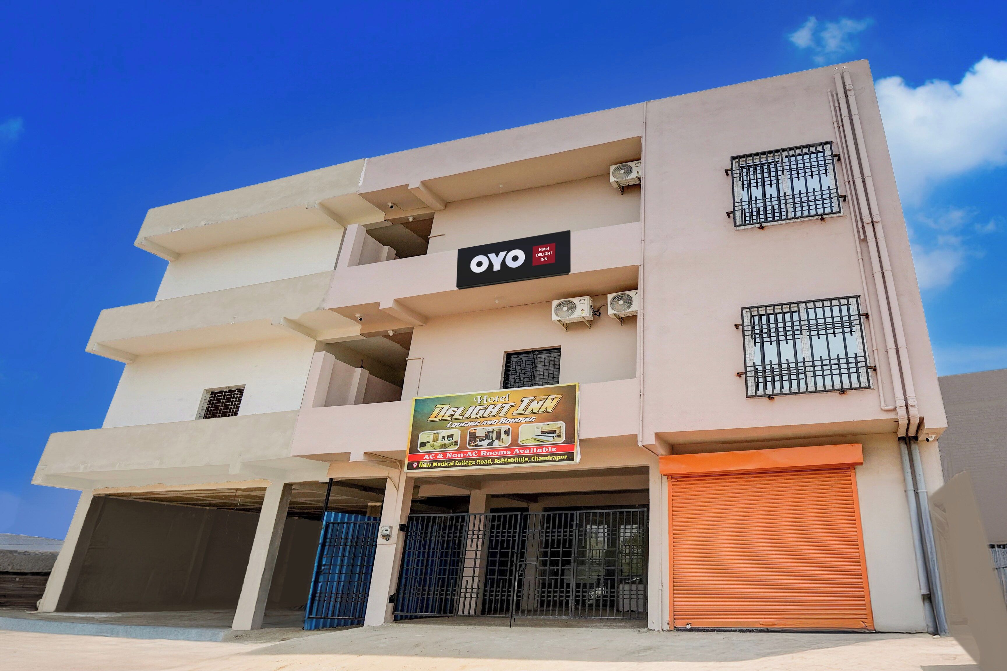 A multi-story hotel with balconies, air conditioning units, and a sign advertising AC & Non-AC rooms.