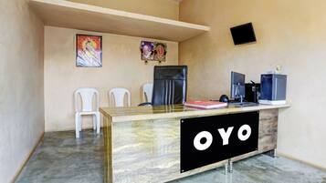 A reception desk with a 'YO' sign, two white chairs, a refrigerator, and a computer setup.