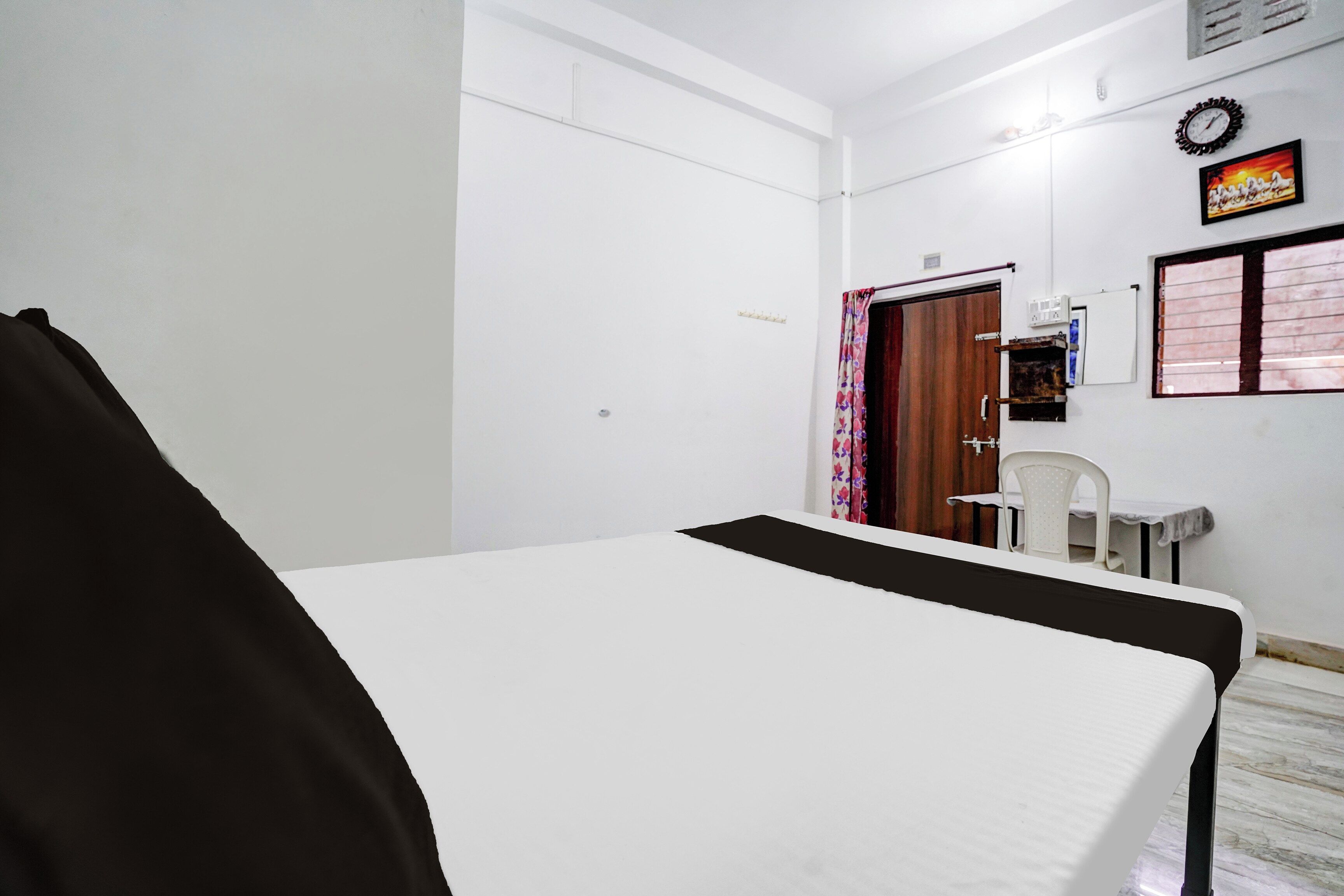 Una habitación de hotel con cama, un escritorio con silla, una puerta de madera y un reloj de pared.