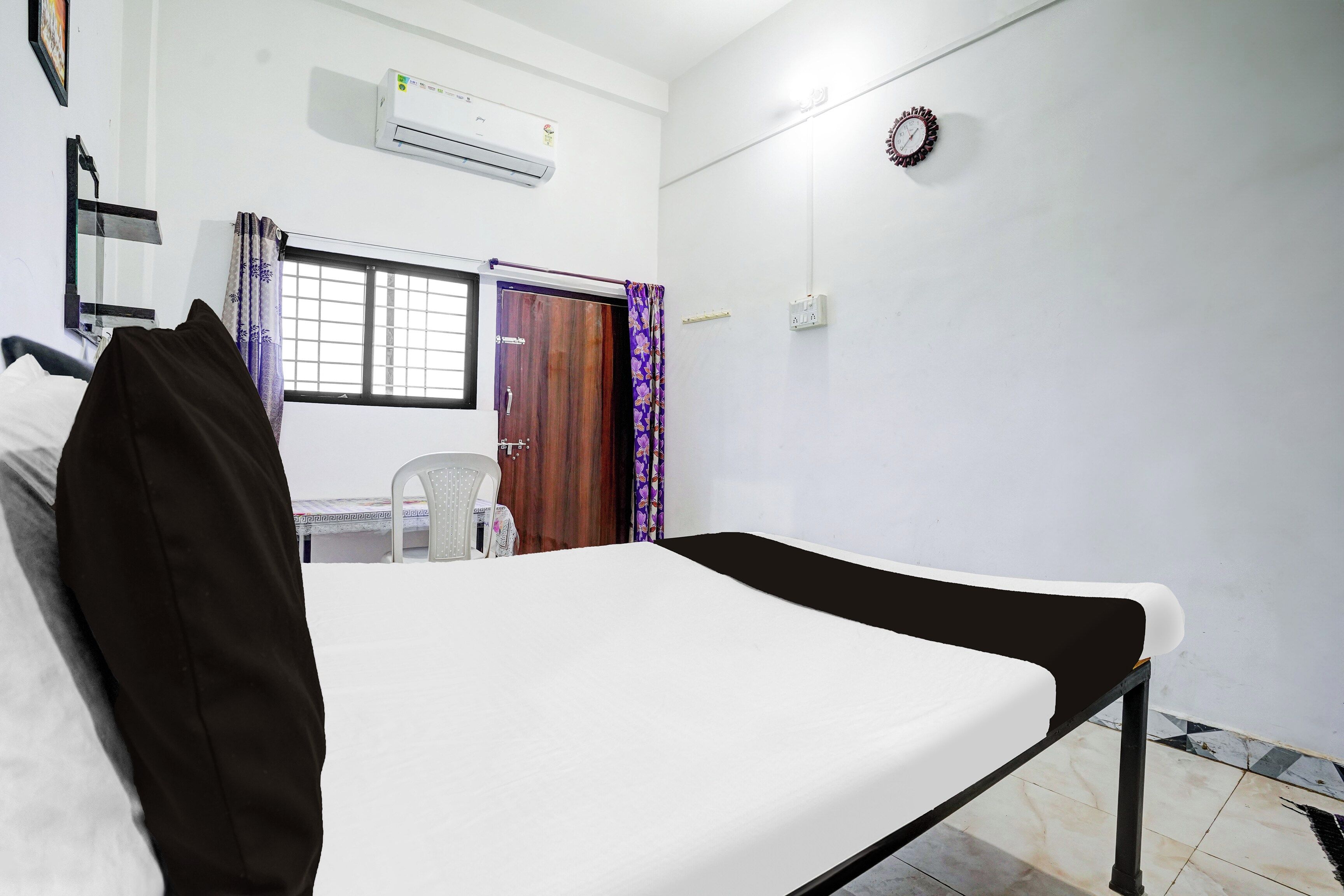 A room with a bed, a window with a view, an air conditioning unit, and a clock on the wall.