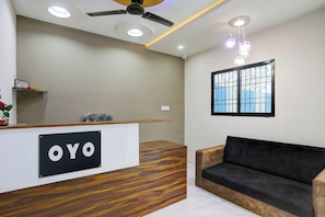 Zona de recepción con mostrador de madera, un sofá negro, ventilador de techo, iluminación empotrada y ventana con vistas.