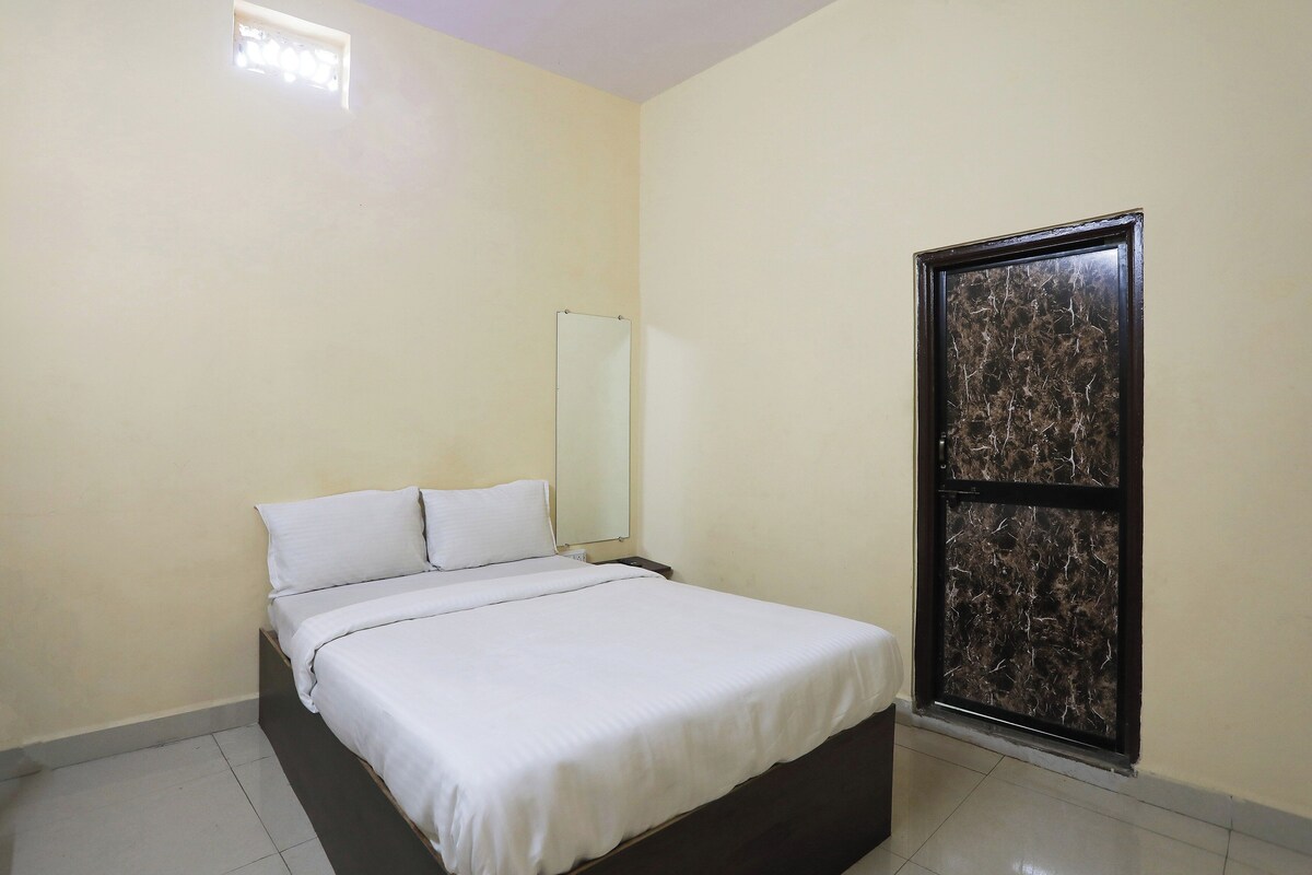 Una habitación sencilla y limpia con una cama, una mesita de noche y un espejo grande.