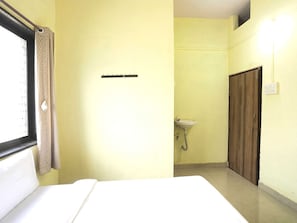 Una habitación con cama, ventana con cortinas, lavamanos y armario.