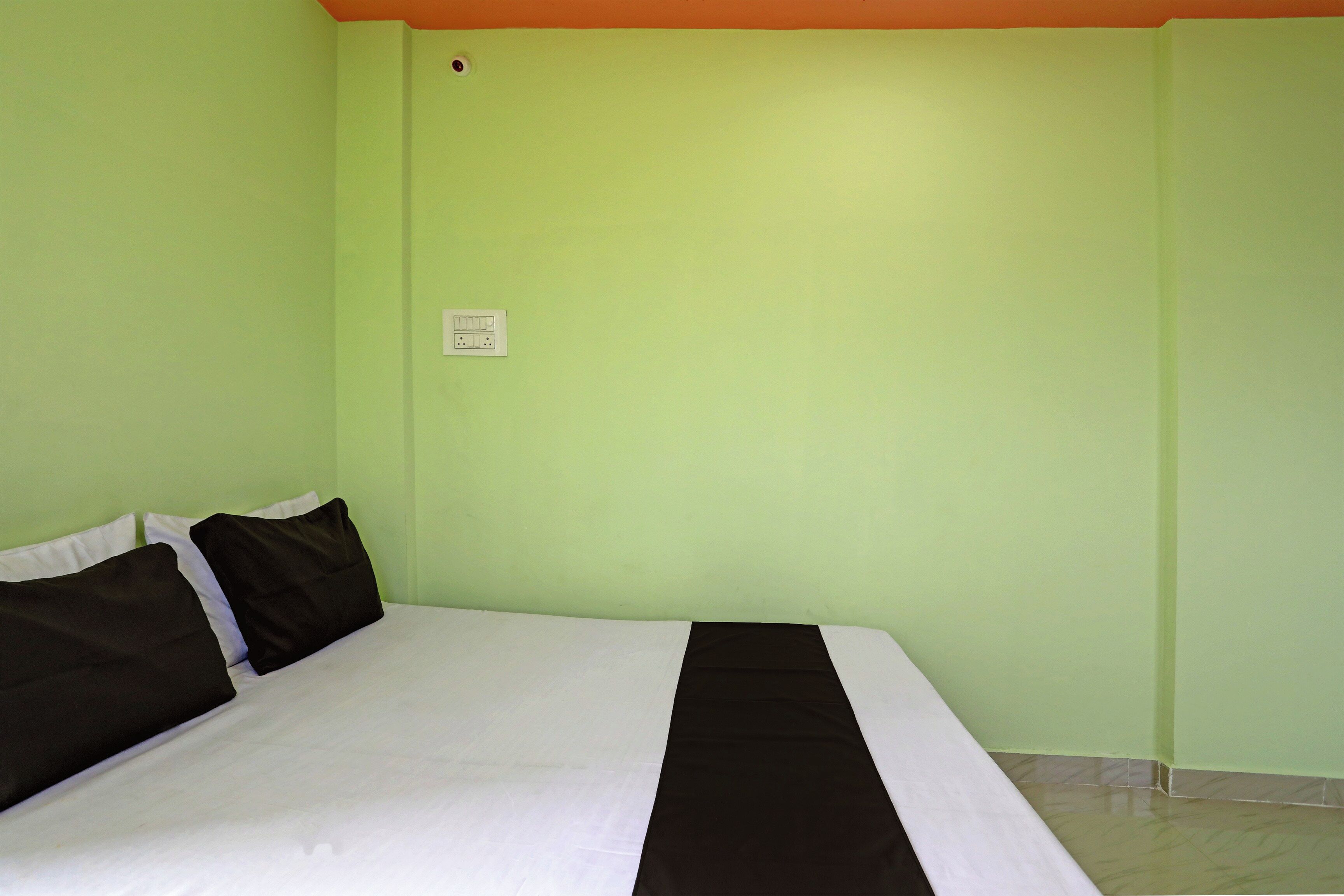 A room with a bed, a power outlet, and a light switch on the wall.