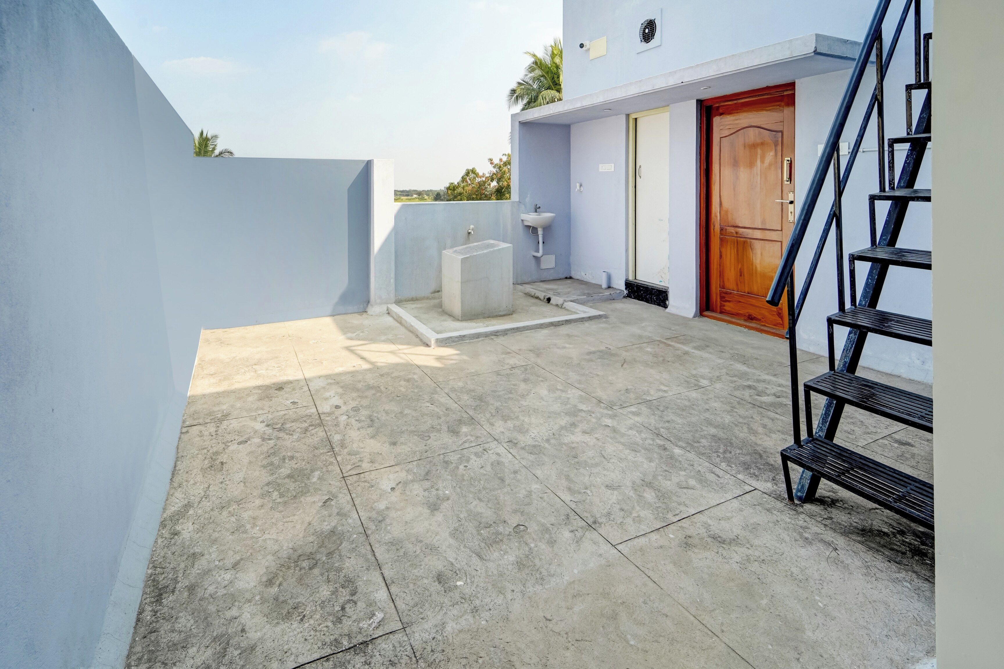 Una terraza con piso de concreto, una puerta de madera, un lavamanos blanco y una escalera de metal.