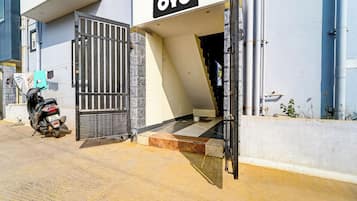 Een gebouwtoegang met een metalen poort, een motorfiets die er geparkeerd staat, en een trap naar de ingang.