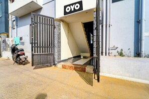 A building entrance with a metal gate, a motorcycle parked outside, and a staircase leading to the entrance.