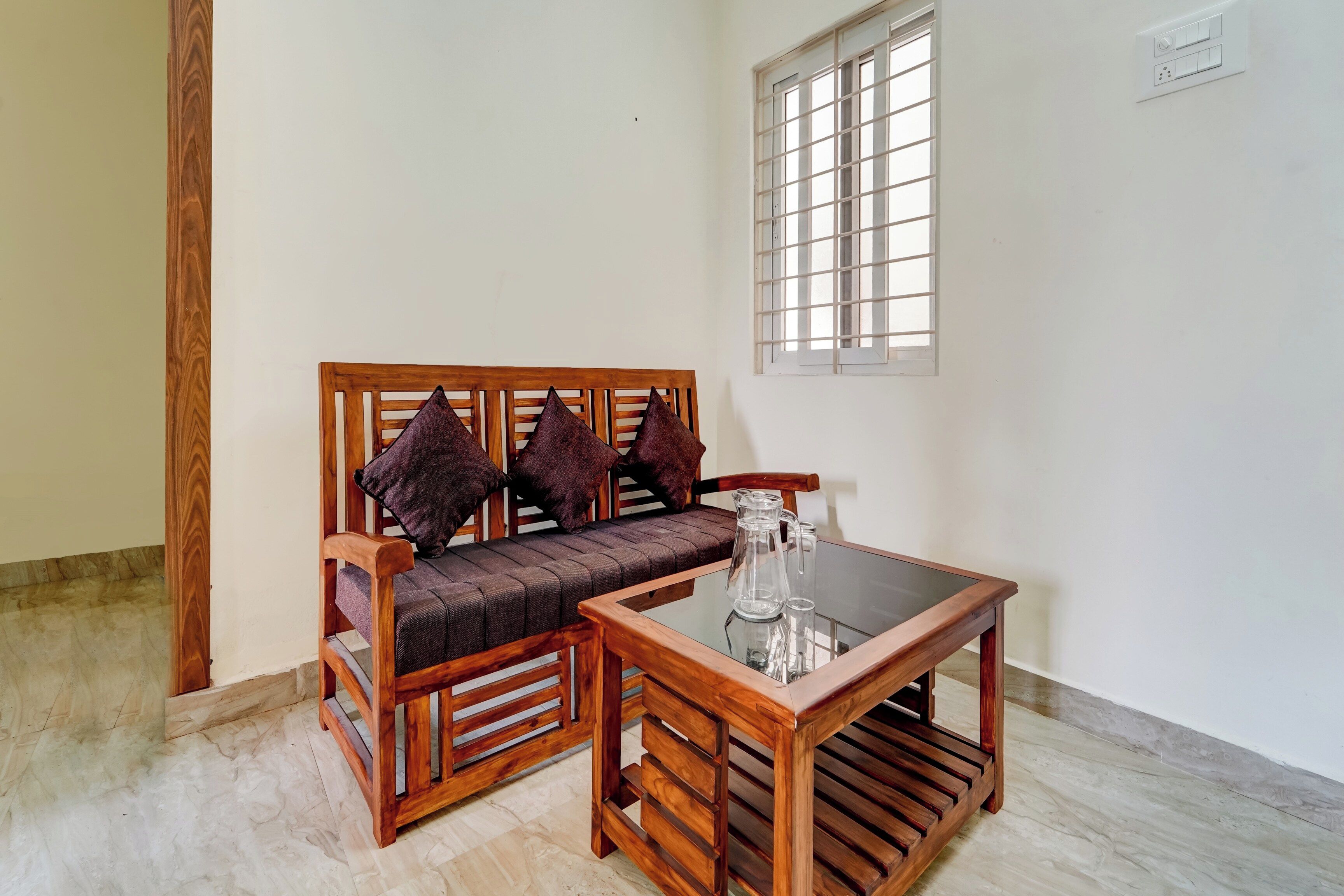 A wooden sofa with cushions, a glass-top table, and a window with bars.
