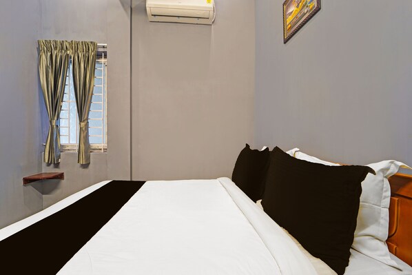 A hotel room with a bed, a window with curtains, an air conditioning unit, and a wall-mounted artwork.