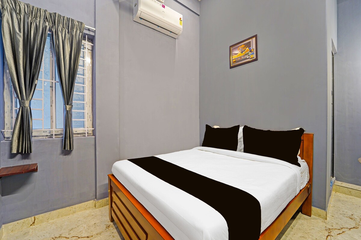 A bedroom with a bed, a window with curtains, an air conditioning unit, and a painting on the wall.