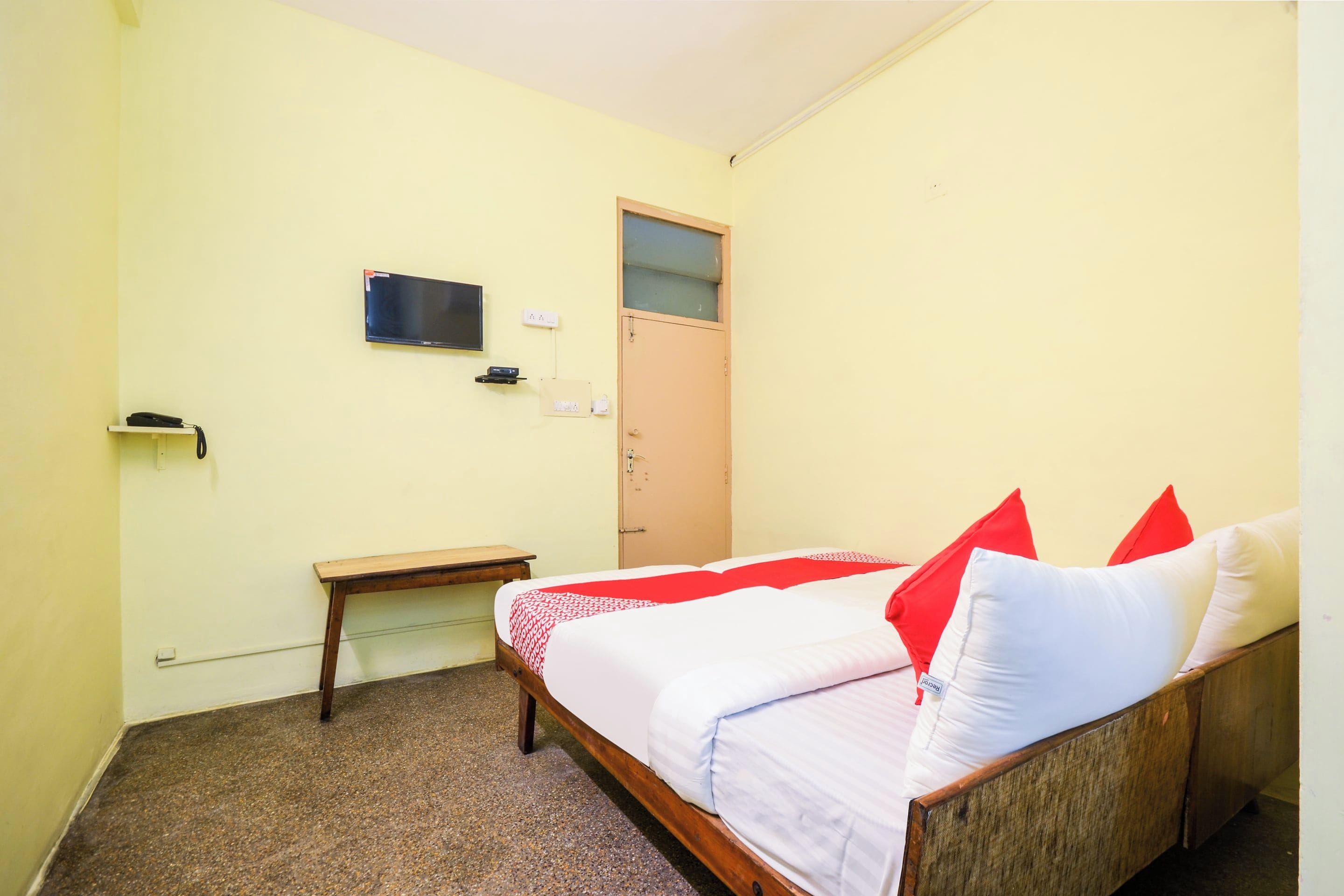 A small, single-bed room with a wooden bed, a desk, a television, and a door.