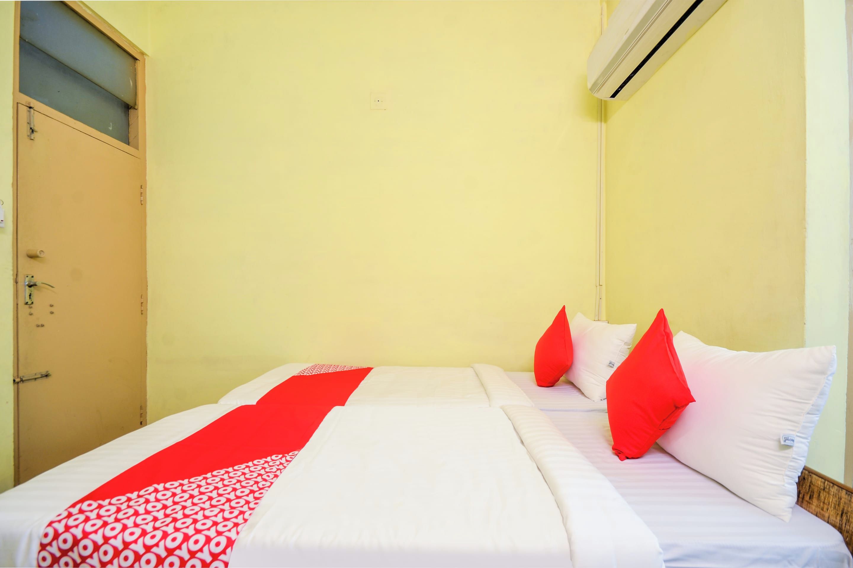 A hotel room with a bed, a window with blinds, an air conditioning unit, and a door.