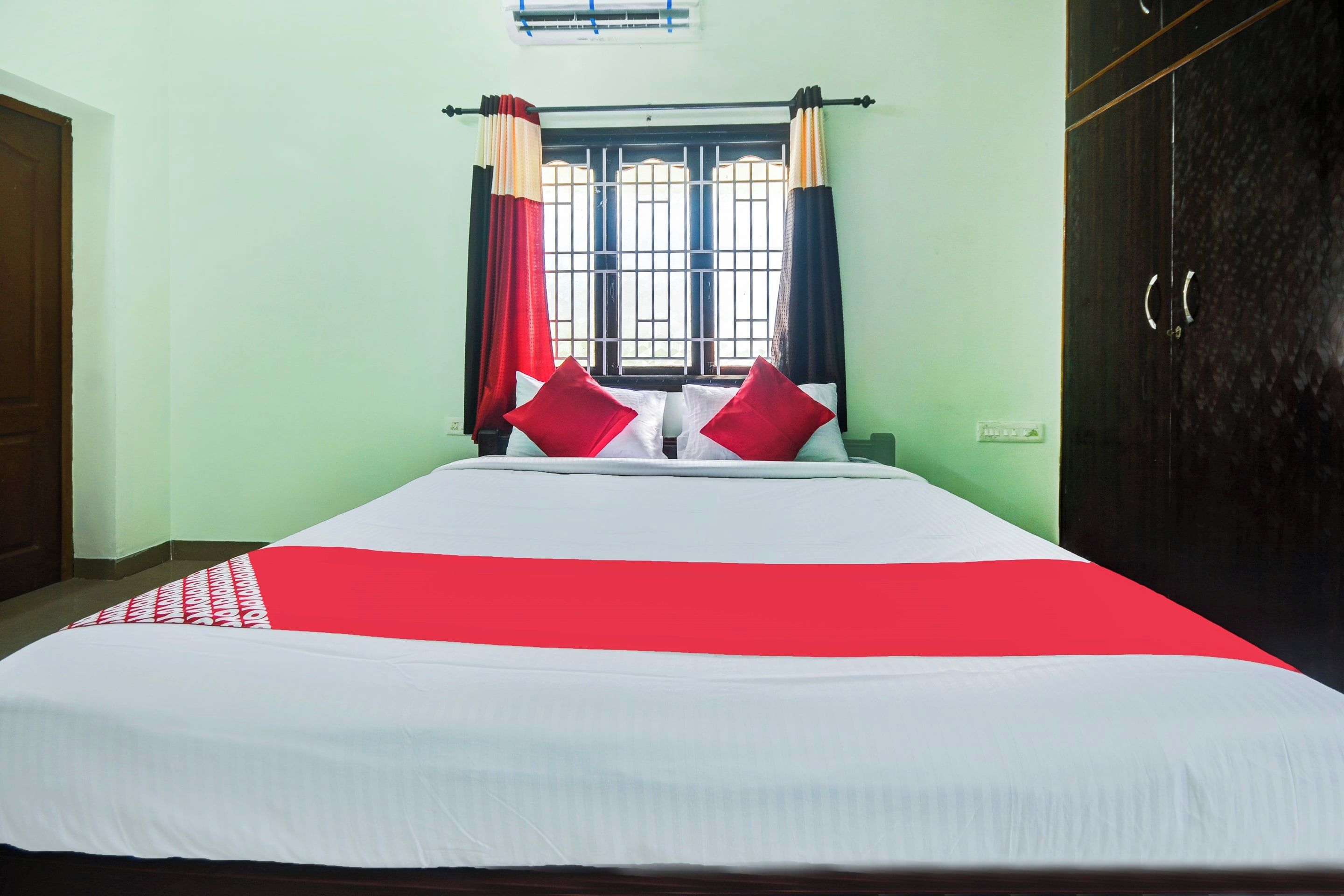 A bed with a white and red bedspread, two red pillows, and a window with curtains.