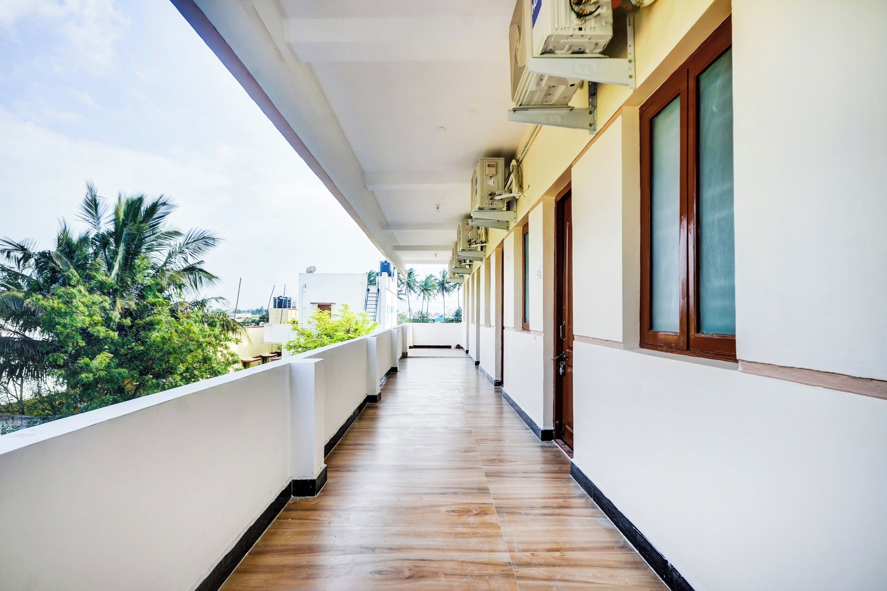 A corridor with a wooden floor, white walls, and a balcony with a view of greenery.