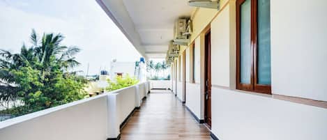 A corridor with a wooden floor, white walls, and a balcony with a view of greenery.