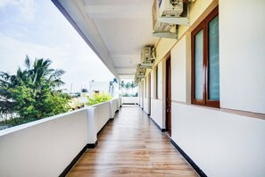 A corridor with a wooden floor, white walls, and a balcony with a view of greenery. - Hotel O Aruthraa Residency (Coimbatore)