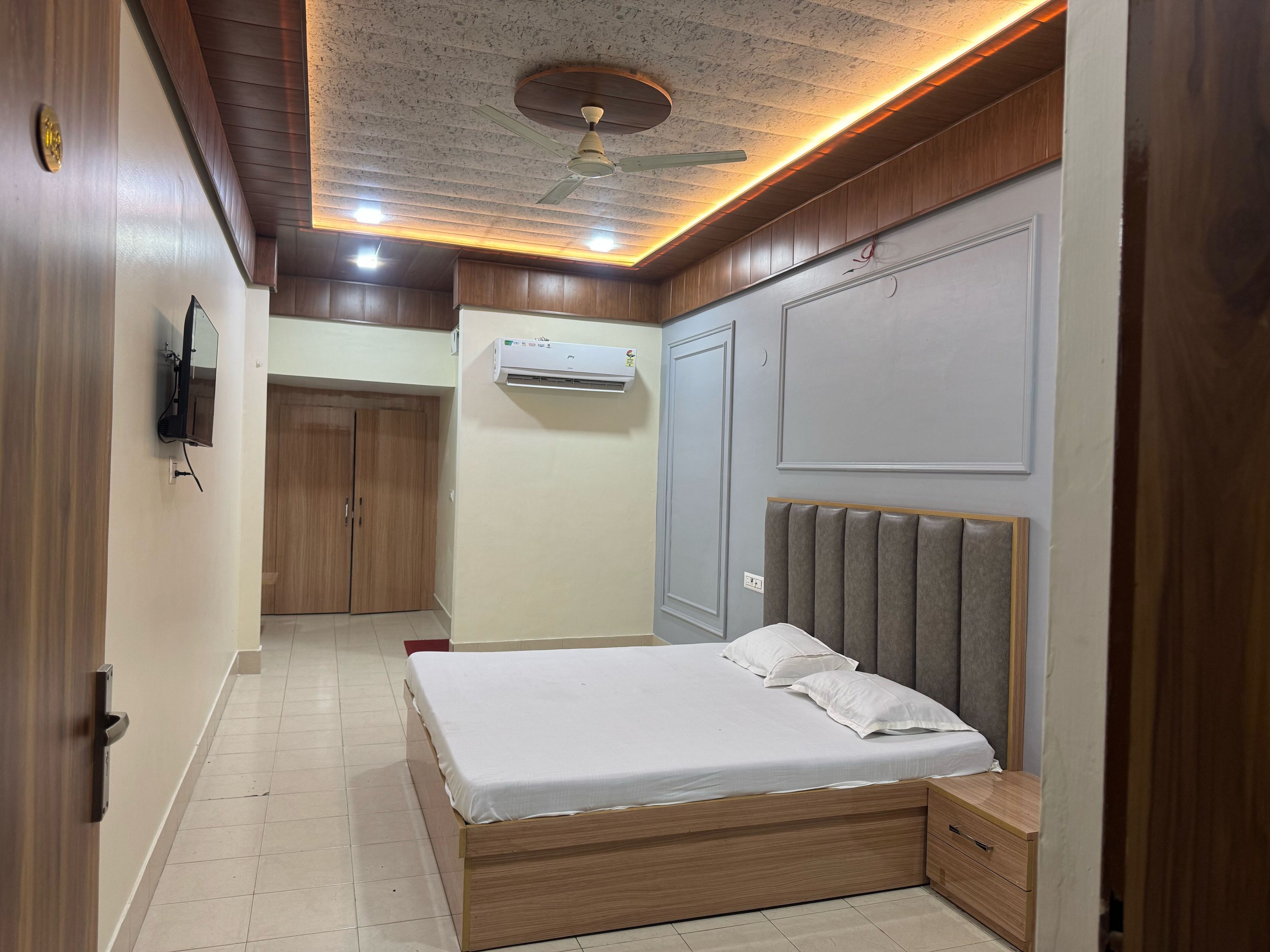Ein Schlafzimmer mit einem Bett, einer Klimaanlage, einem Deckenventilator und einem Fernseher an der Wand.