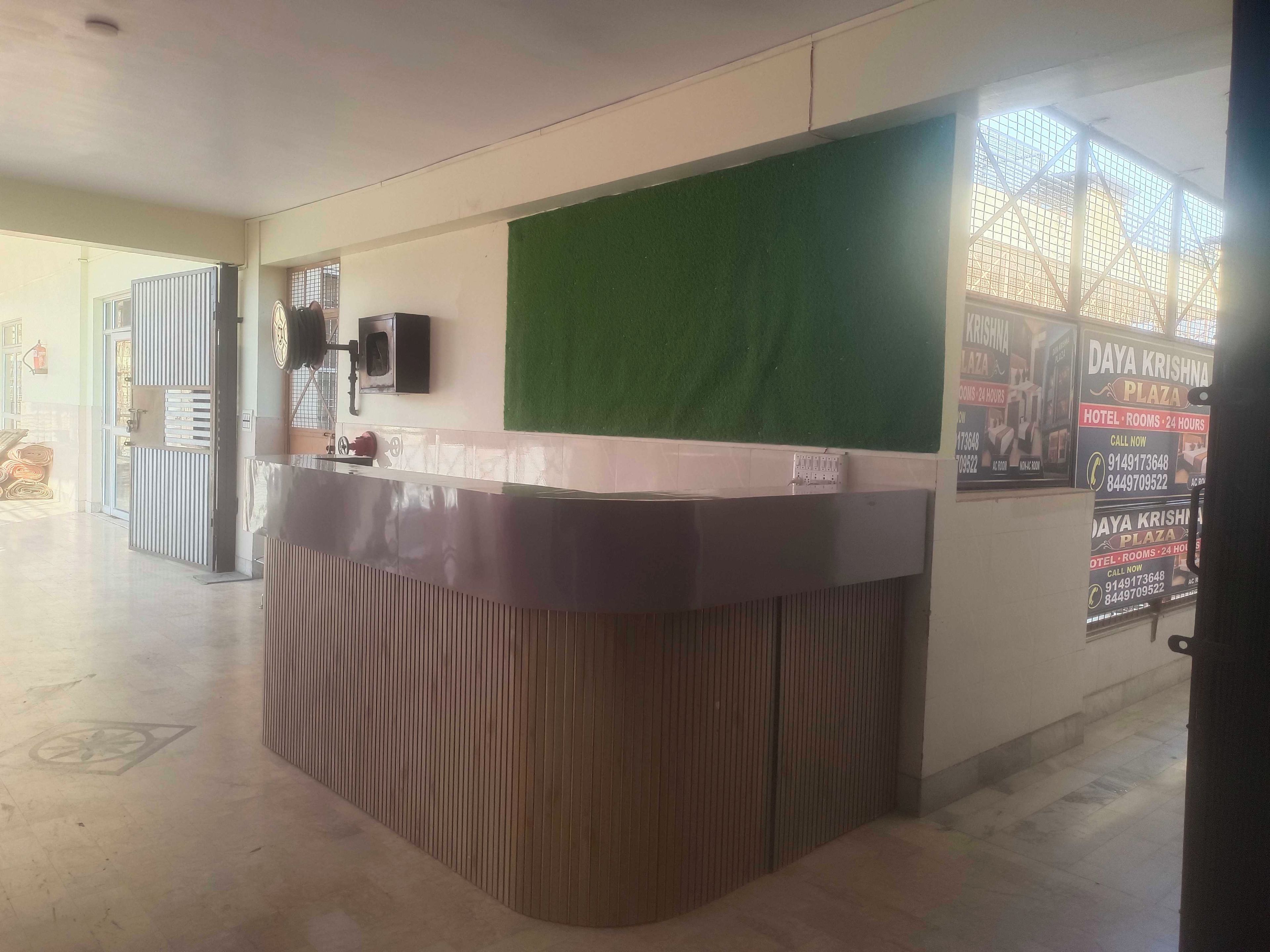 Zona de recepción con mostrador, pared verde y cartel publicitario de un hotel.