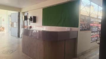 Zona de recepción con mostrador, pared verde y cartel publicitario de un hotel.