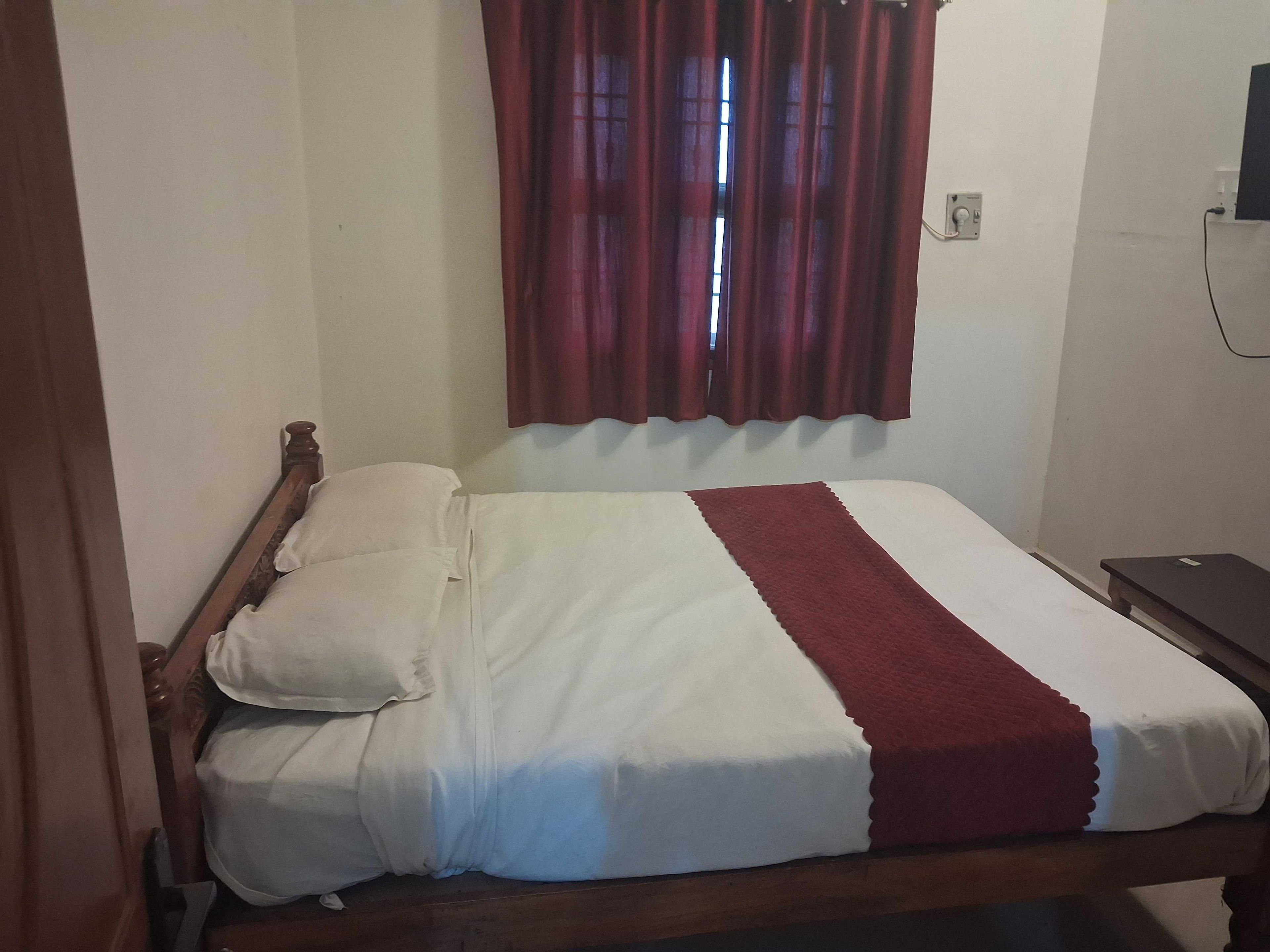Una cama individual con estructura de madera, ropa de cama blanca y una manta roja.