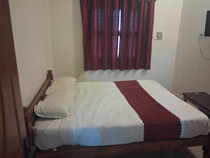 Una cama individual con estructura de madera, ropa de cama blanca y una manta roja.