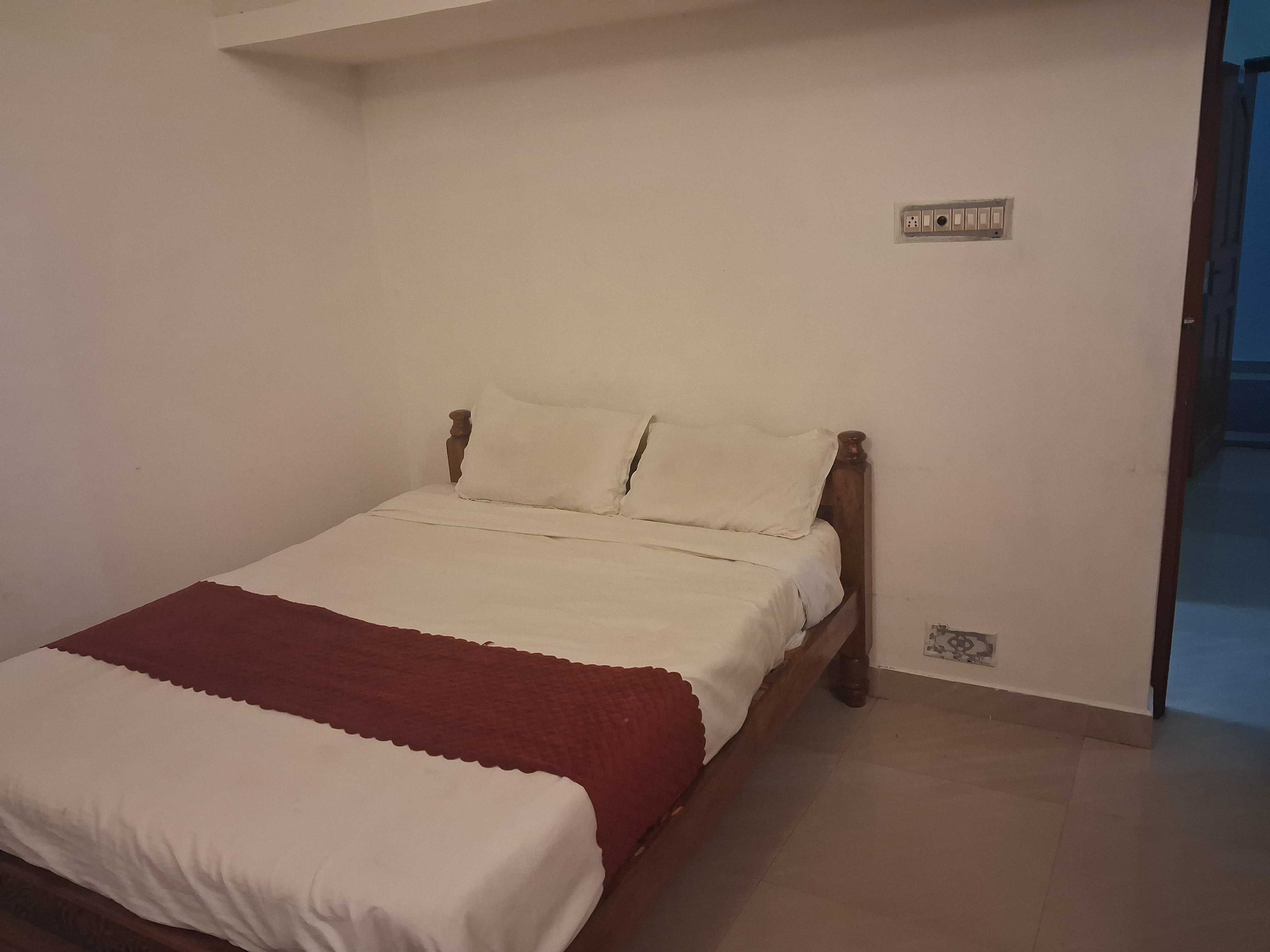 Una cama individual con estructura de madera, ropa de cama blanca y una manta roja.