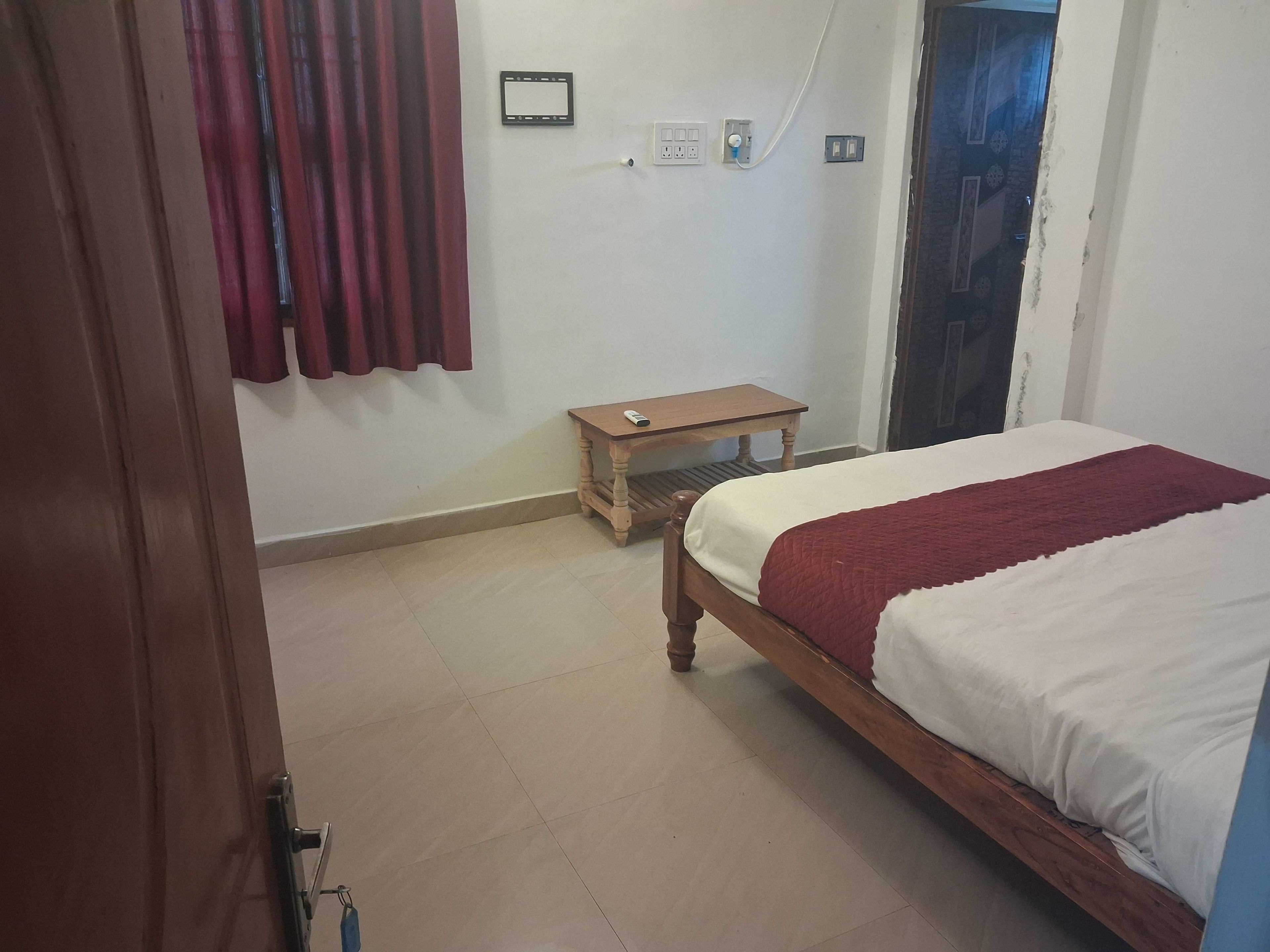 A bedroom with a bed, a small wooden table, a wall socket, and a curtain.