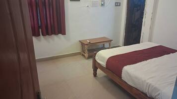 A bedroom with a bed, a small wooden table, a wall socket, and a curtain.