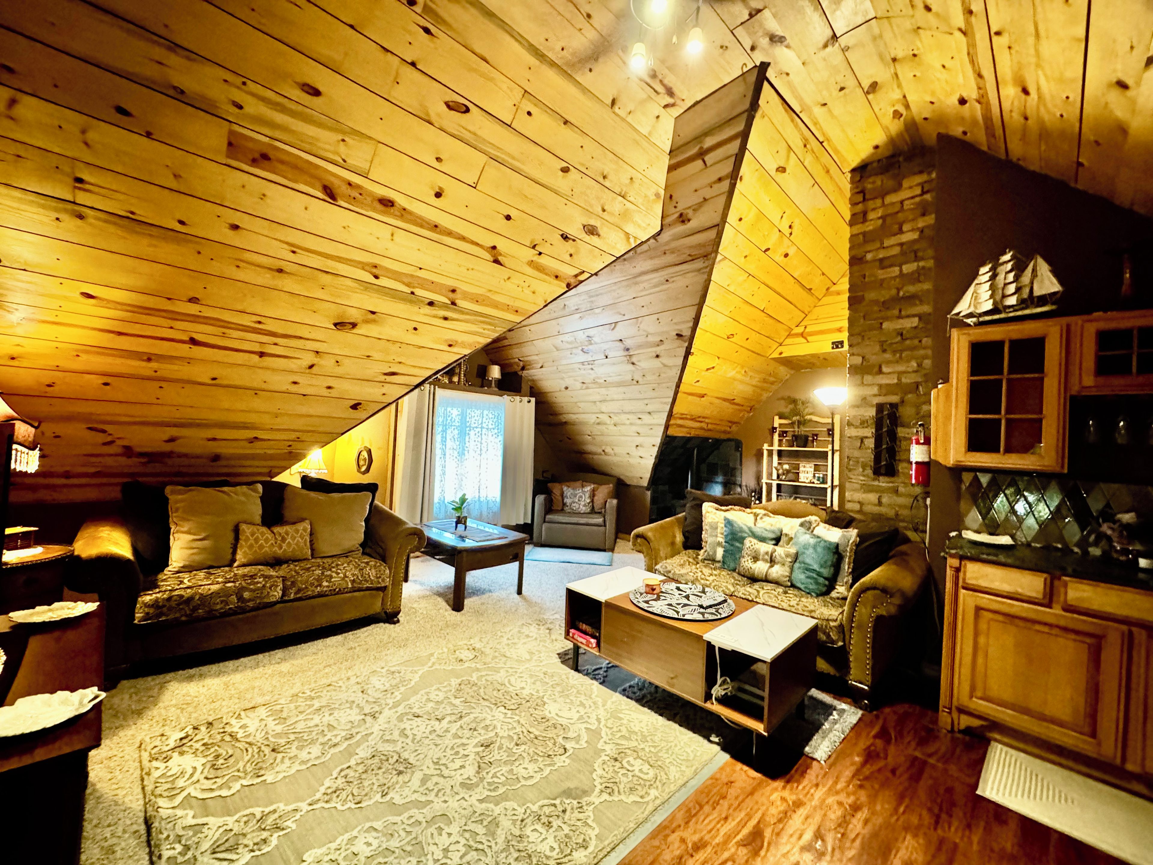 A cozy attic room with wooden beams, a fireplace, and a dining area with a table and chairs.