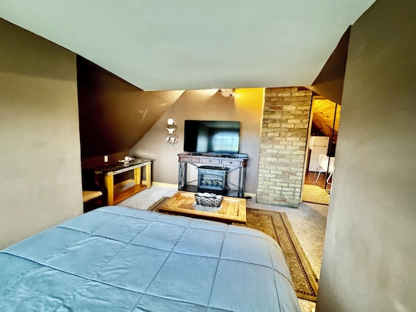 A bedroom with a bed, a dresser, a television, and a brick wall.